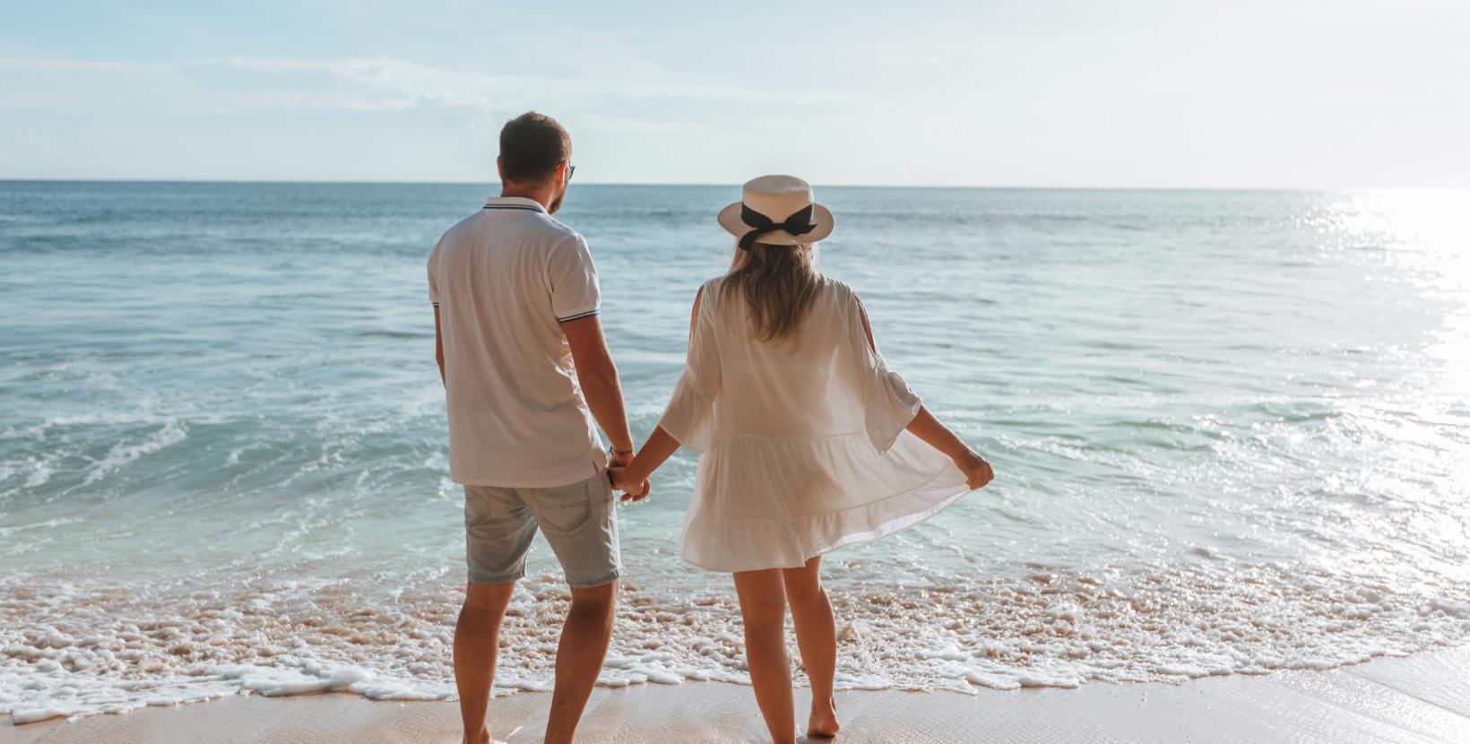 Coppia romantica in spiaggia, mano nella mano, guardando il mare.