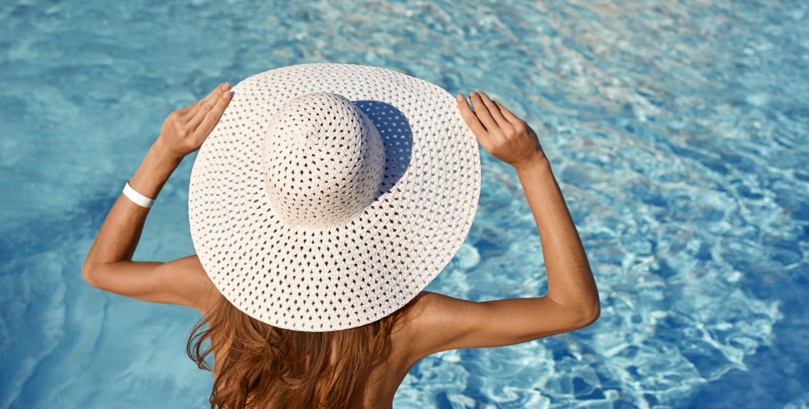 Persona con cappello bianco di paglia, vista di spalle, davanti a una piscina.