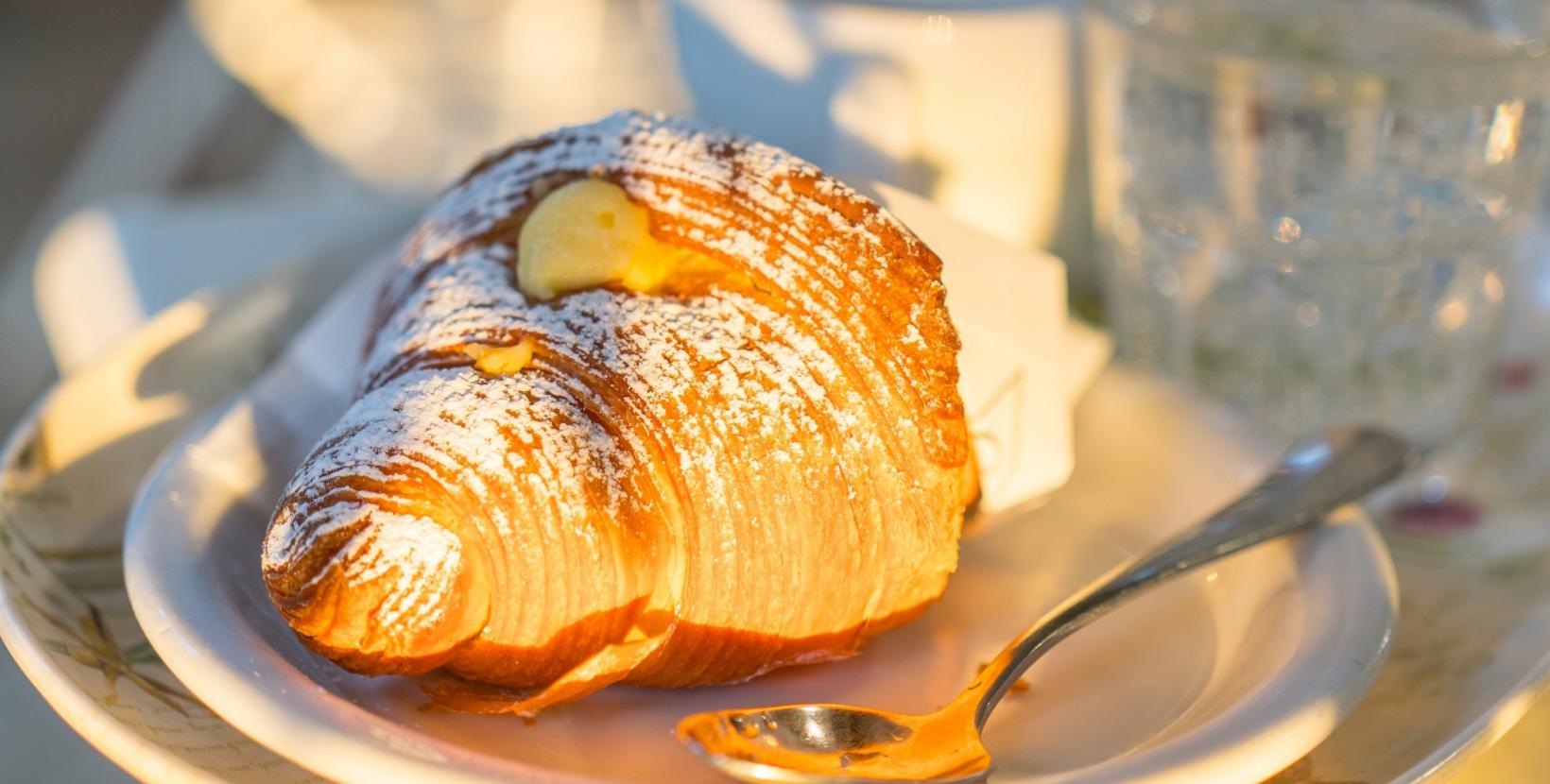 Cornetto alla crema con zucchero a velo, servito su un piatto con cucchiaino.
