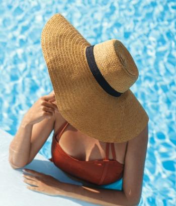 Donna in piscina con cappello di paglia e costume rosso, rilassata al sole.