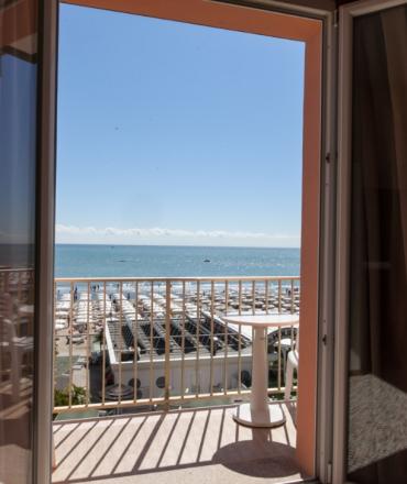 Vista mare da un balcone con tavolino, ombrelloni sulla spiaggia e cielo sereno.