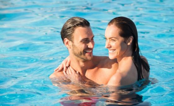 Coppia sorridente abbracciata in piscina, godendo una giornata di sole e relax.