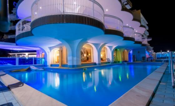 Piscina illuminata di notte con architettura moderna e balconi curvilinei.