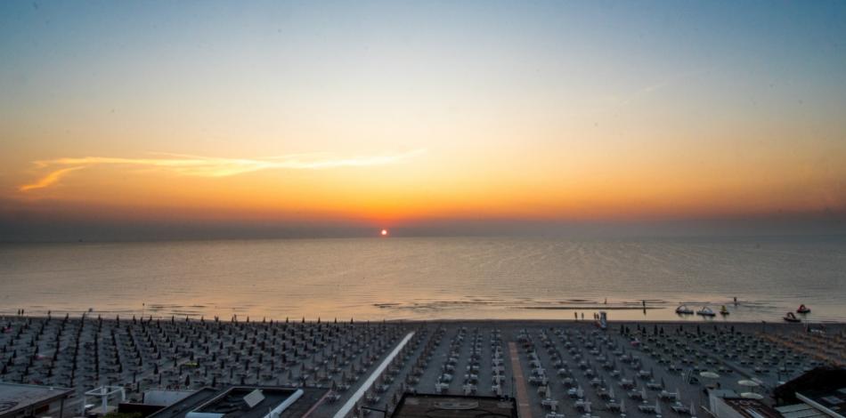 Spiaggia al tramonto con ombrelloni e mare calmo, atmosfera serena e rilassante.